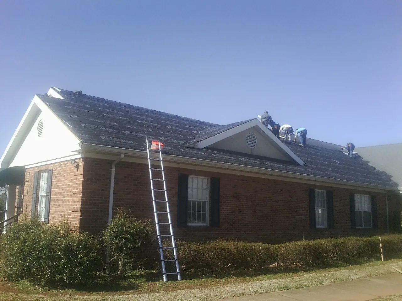 Crew tearing shingles off a brick ranch roof with a ladder set — Metal Roof Repair work by our crew in West Terre Haute