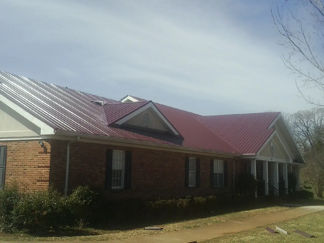 Red metal roof with gabled entries on a long brick building, from a Hail Damage Roof Repair job in West Terre Haute