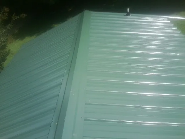 New green metal panels meeting at the ridge of a roof — Flat Roof Repair work by our crew in West Terre Haute