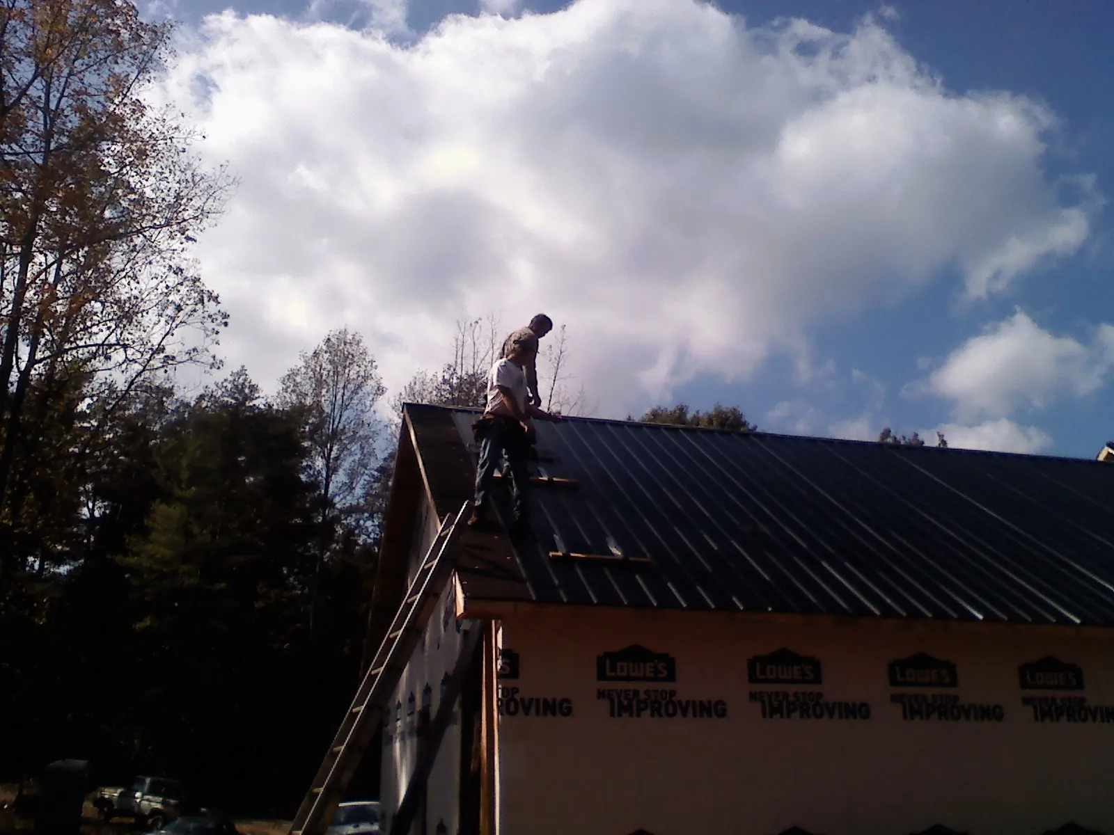Roofer fastening dark metal panels high against a cloudy sky, from a Roof Inspection job in West Terre Haute