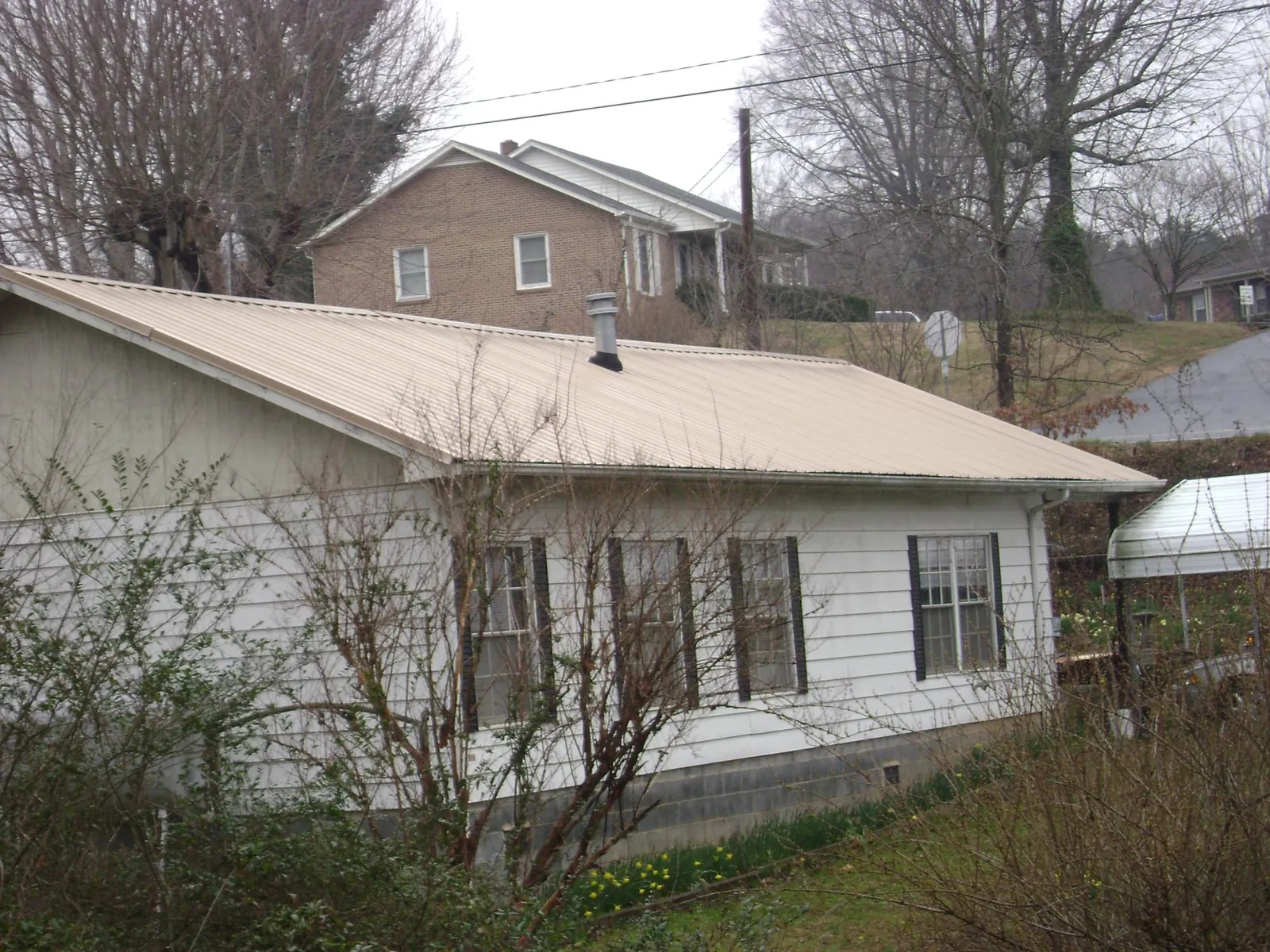 Tan metal roof on a white sided house set into a hillside — Commercial Roofing by Roofing Brothers in West Terre Haute